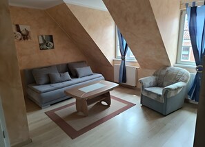 A modern living room with a sofa, armchair, and coffee table, featuring a sloped ceiling and large windows with curtains.