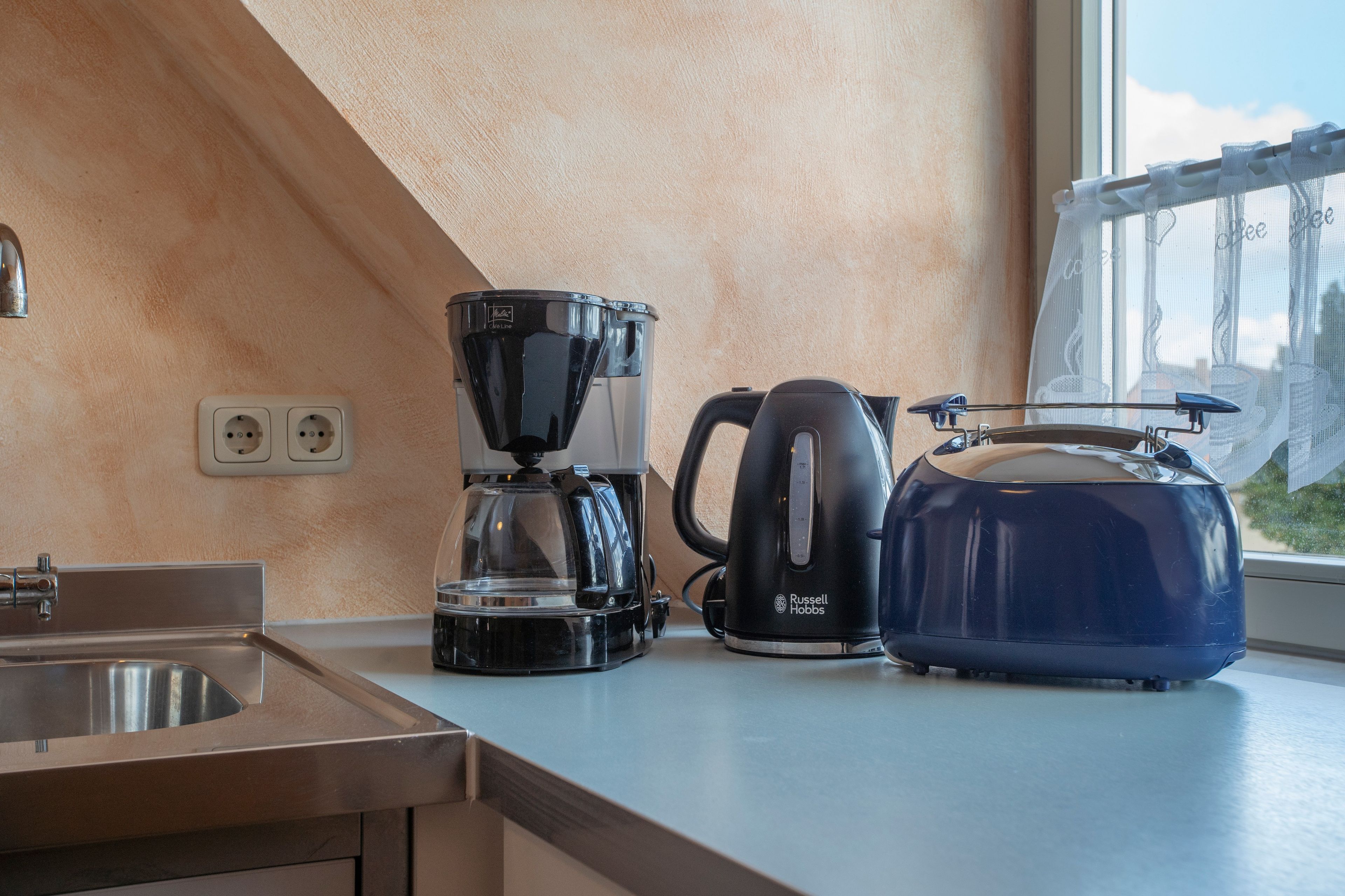 A kitchen with a coffee maker, kettle, and a toaster on the counter.