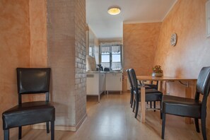 A compact kitchen with a dining area, featuring a brick column, a wooden dining table with chairs, and a small potted plant. - Apartment 'Fewo Steuerboard' with Shared Terrace, Shared Garden and Wi-Fi (Röbel)
