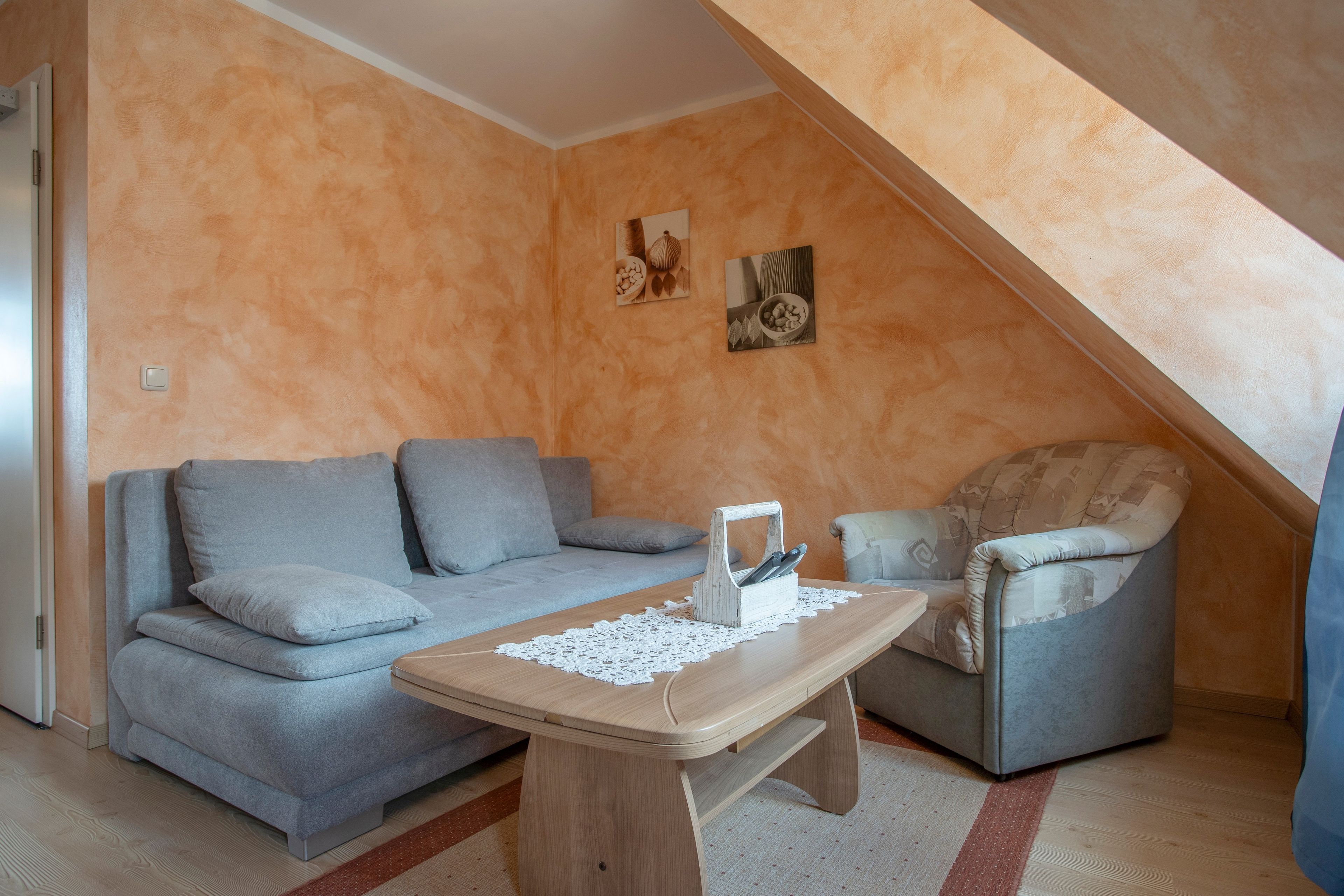 Ein gemütliches Wohnzimmer mit einem grauen Sofa, einem Holztisch und einem gemusterten Sessel.