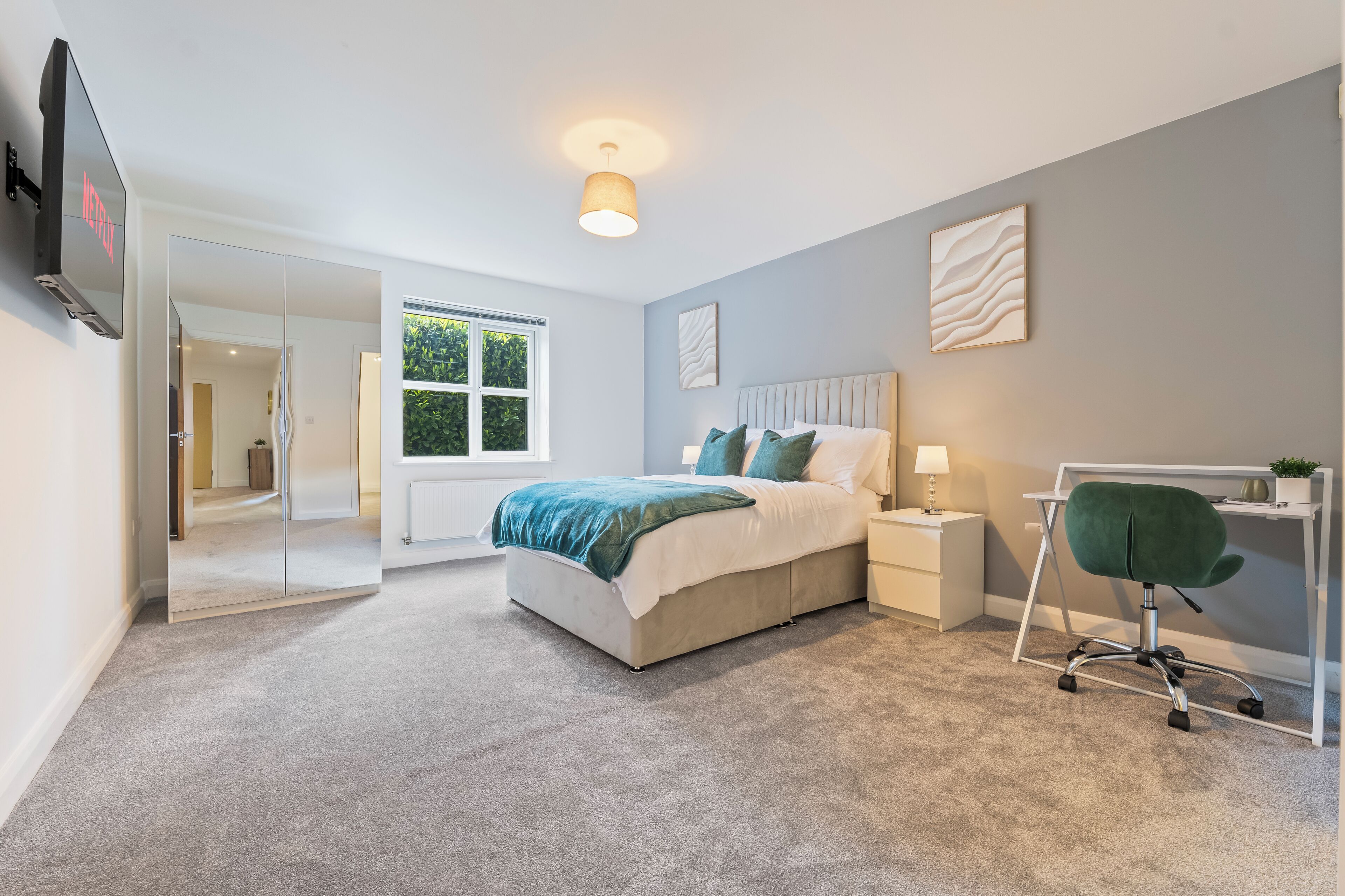 A modern bedroom with a bed, bedside table, chair, and a TV mounted on the wall.