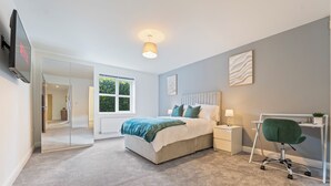 A modern bedroom with a bed, bedside table, chair, and a TV mounted on the wall. - Luxury 2 Bed open plan Apartment | prime location (Wythenshawe)