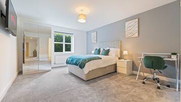 A modern bedroom with a bed, bedside table, chair, and a TV mounted on the wall.