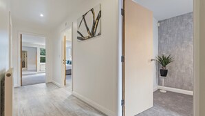 A hallway with a light wooden floor, a door with a modern handle, a wall-mounted abstract art piece, and a potted plant. - Luxury 2 Bed open plan Apartment | prime location (Wythenshawe)