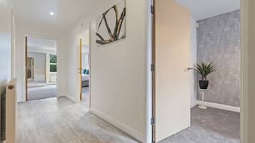 A hallway with a light wooden floor, a door with a modern handle, a wall-mounted abstract art piece, and a potted plant.
