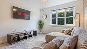 A modern living room with a flat-screen TV, a sofa, a coffee table, a potted plant, and a large window. - Luxury 2 Bed open plan Apartment | prime location (Wythenshawe)