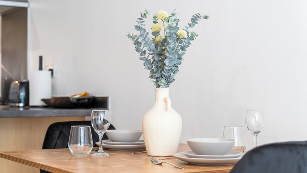 A dining table with a vase of flowers, plates, and glasses. - Luxury 2 Bed open plan Apartment | prime location (Wythenshawe)