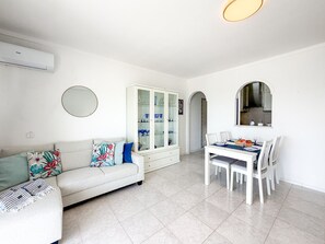 Ein modernes Wohnzimmer mit Sofa, Esstisch, Stühlen, einem Schrank mit Glastüren und einer Klimaanlage.