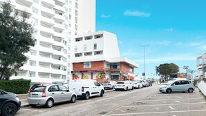 A parking lot with several cars, a supermarket, and a tall white building with balconies. - Apartment Praia Rocha | Sea | Concorde Infinity (Portimão)