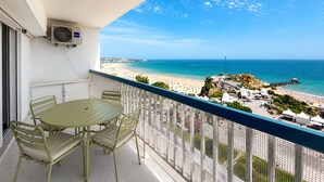 A balcony with a table and chairs, overlooking a beach and ocean. - Apartment Praia Rocha | Sea | Concorde Infinity (Portimão)