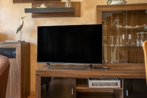 A flat-screen TV on a wooden entertainment center with a glass display cabinet containing wine glasses.