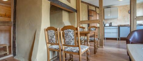A dining area with wooden chairs and a table, a kitchen in the background, and a wooden floor.