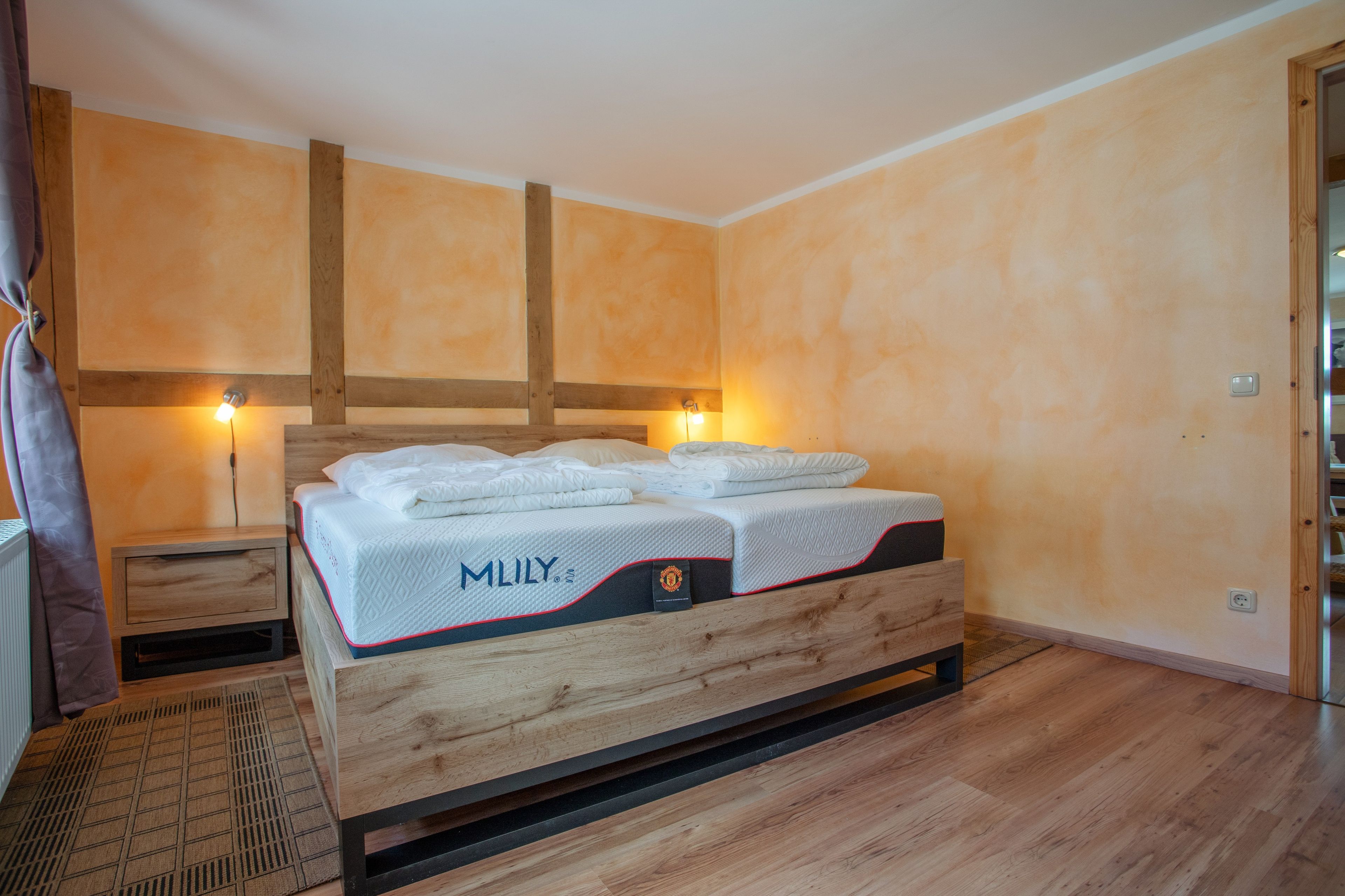 A hotel room with a wooden bed, a nightstand, and a wall-mounted lamp.