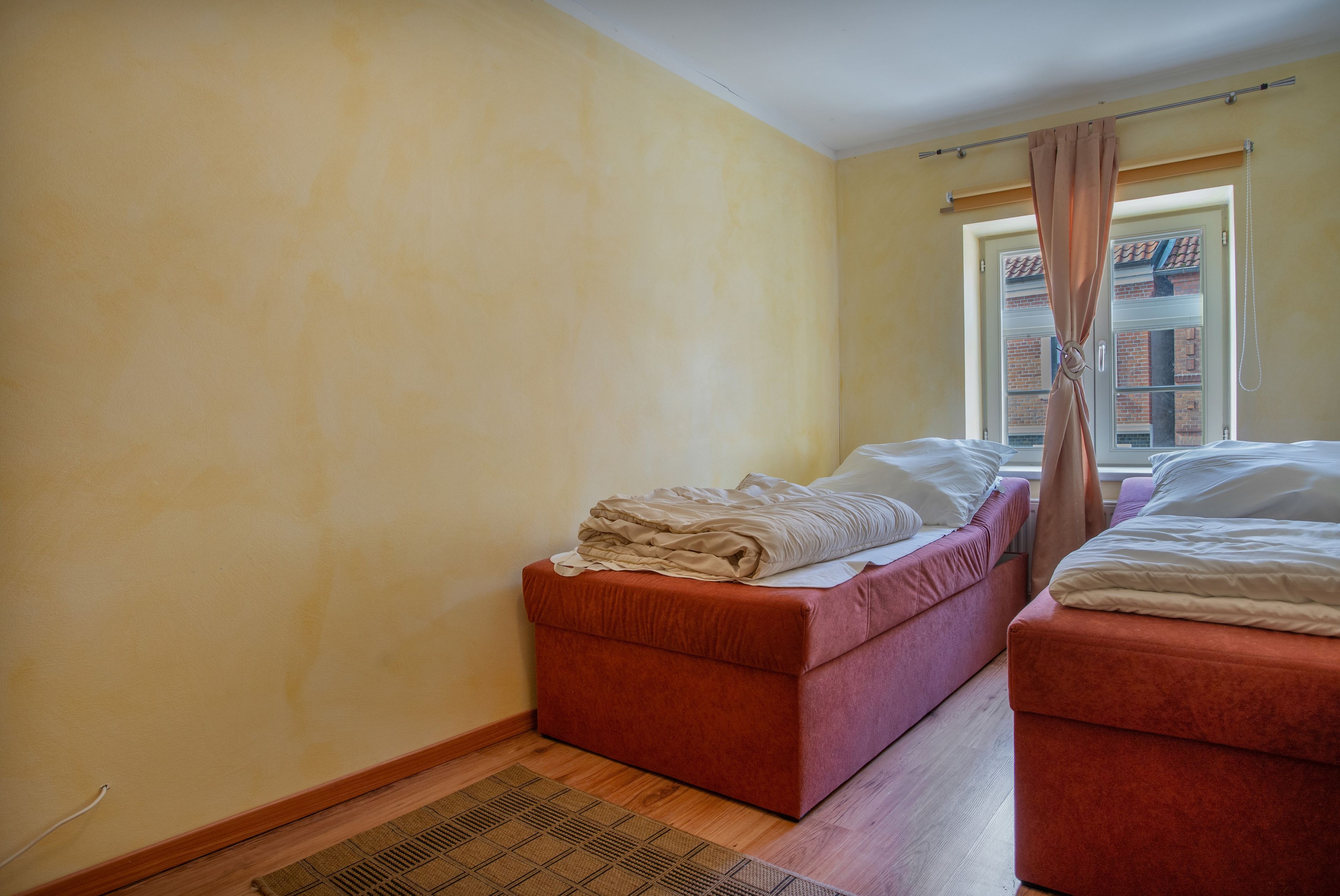 A room with two beds, a small sofa, a window with curtains, and a wooden floor.