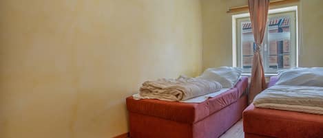 Une chambre avec deux lits, un petit canapé, une fenêtre avec des rideaux et un plancher en bois.
