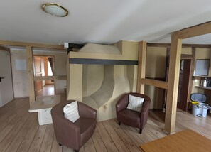 A room with a bunk bed, two leather chairs, a wooden table, and a ceiling light fixture.