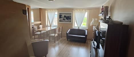 A room with a dining table, chairs, a sofa, a TV, and a cabinet.