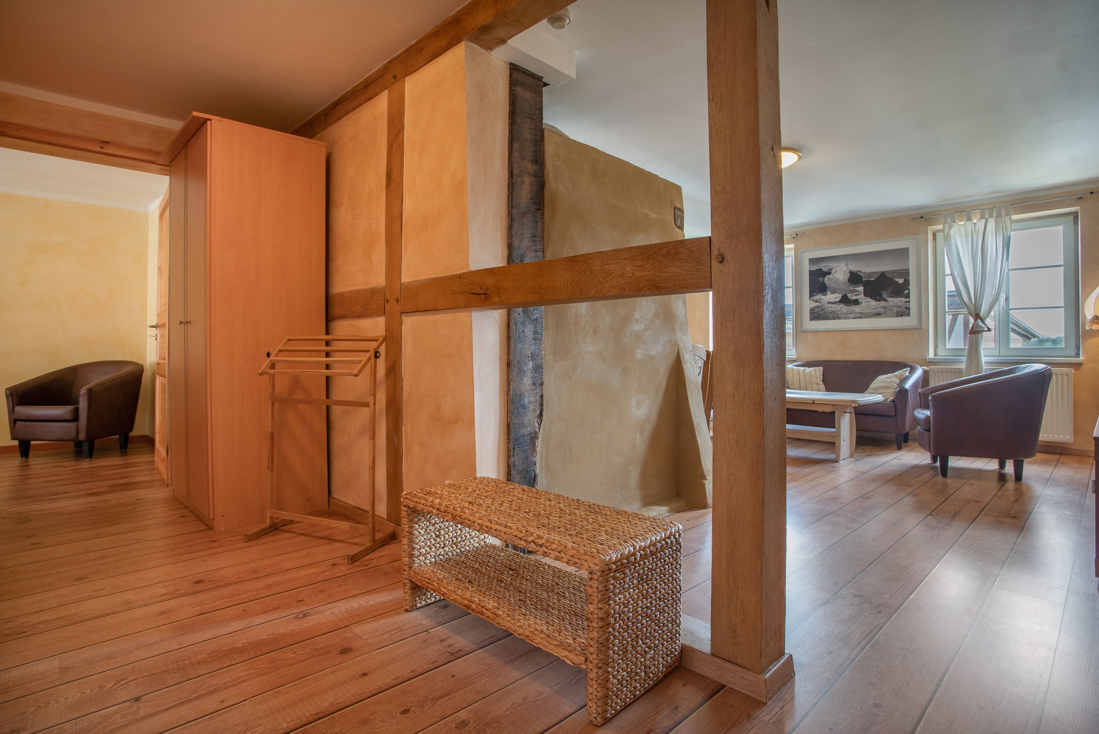 A room with wooden flooring, a bench, a sofa, and a window with curtains.