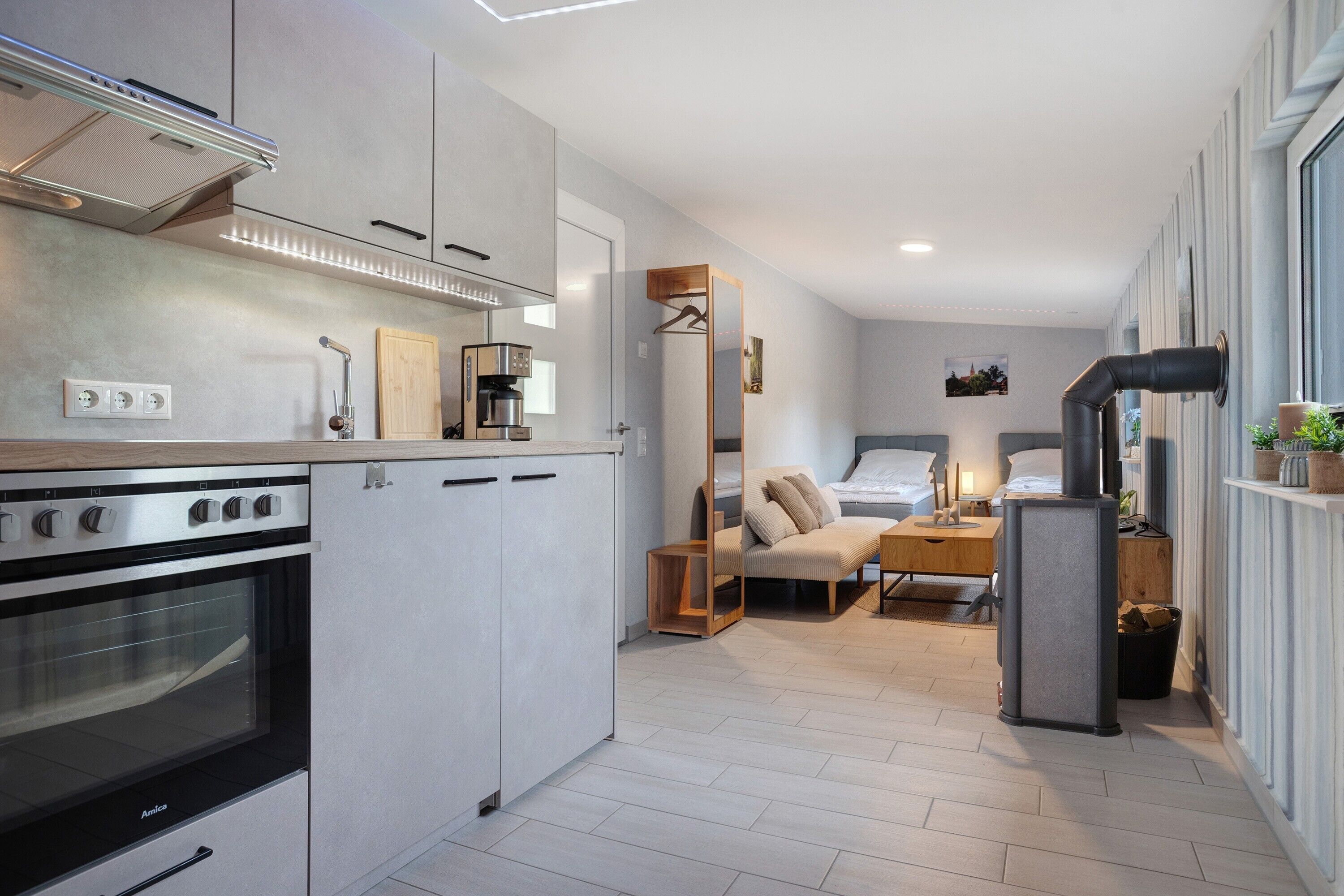 A compact kitchen with modern appliances, a dining area with a sofa and table, and a bedroom with a bed and bedside table.