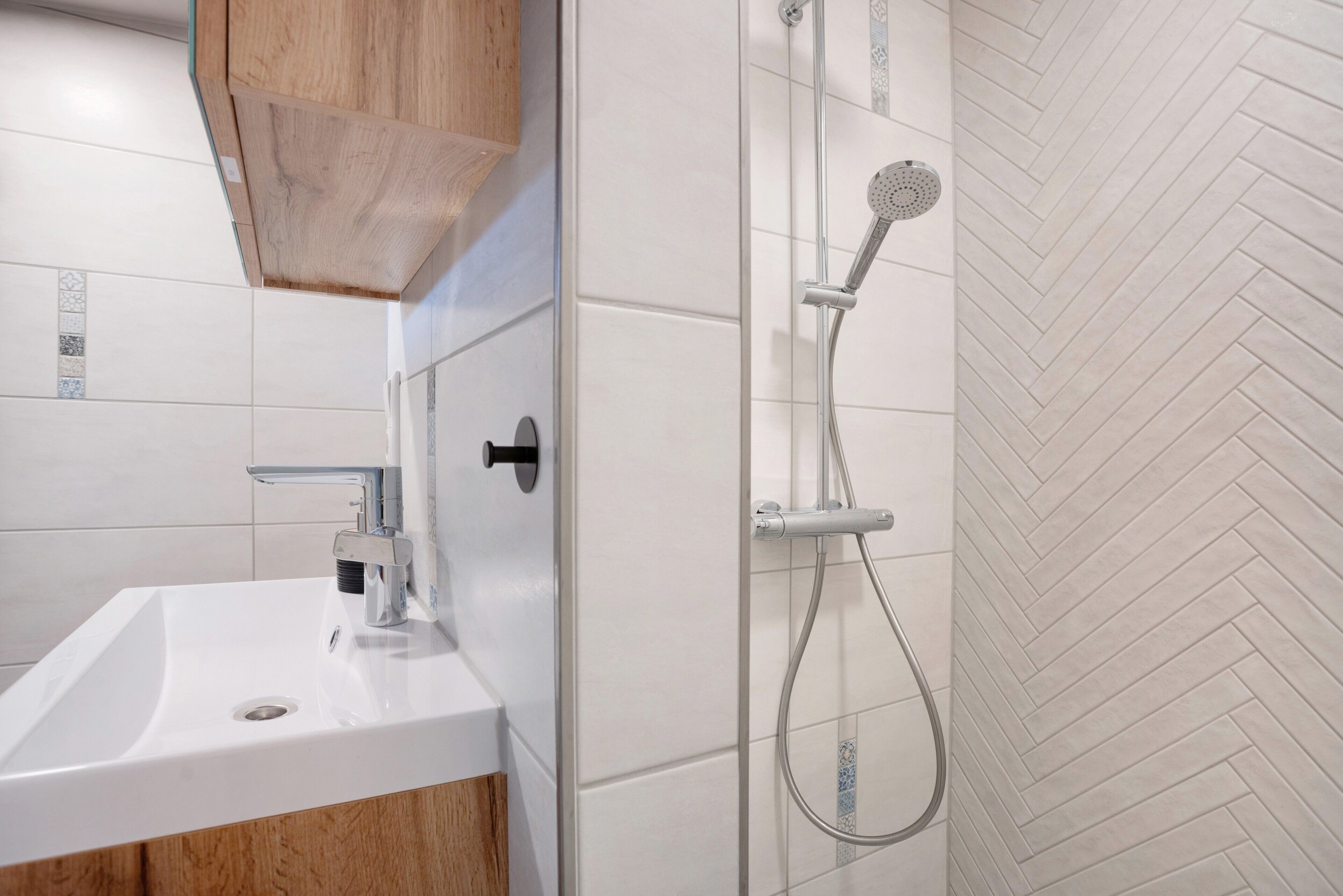 A bathroom with a white sink, wooden cabinet, and a shower with a herringbone tile pattern.