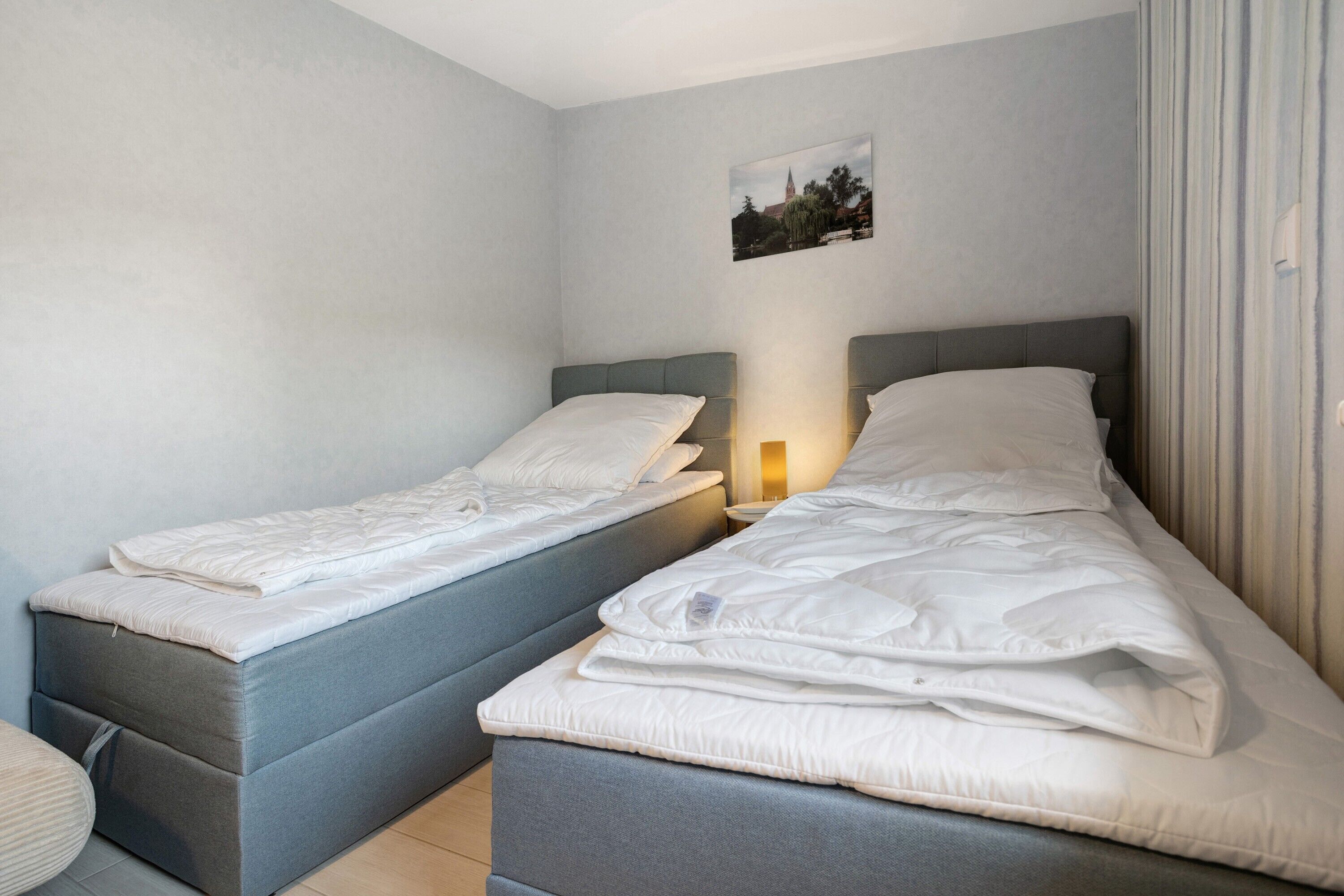 A room with two beds, a small table, and a picture on the wall.
