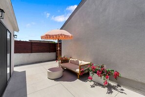 A patio with a cushioned seating area, a round table, and a decorative umbrella. - Vista Studio Oasis | Patio, Beaches & Local Dining (Vista)