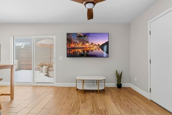 Ein modernes Wohnzimmer mit einem Wand-Fernseher, einem runden weißen Tisch mit goldenen Beinen und einem Deckenventilator.
