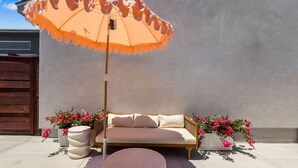 Een terras met een bank, een parasol en plantenpotten.