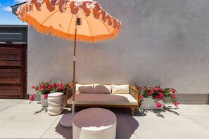 An outdoor seating area with a sofa, an umbrella, and potted plants. - Vista Studio Oasis | Patio, Beaches & Local Dining (Vista)