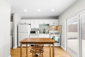 A compact kitchen with white cabinets, a wooden table, and a wicker chair. - Vista Studio Oasis | Patio, Beaches & Local Dining (Vista)