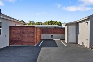 A parking area with a wooden fence, a garage door, and a building with a light-colored exterior. - Vista Studio Oasis | Patio, Beaches & Local Dining (Vista)