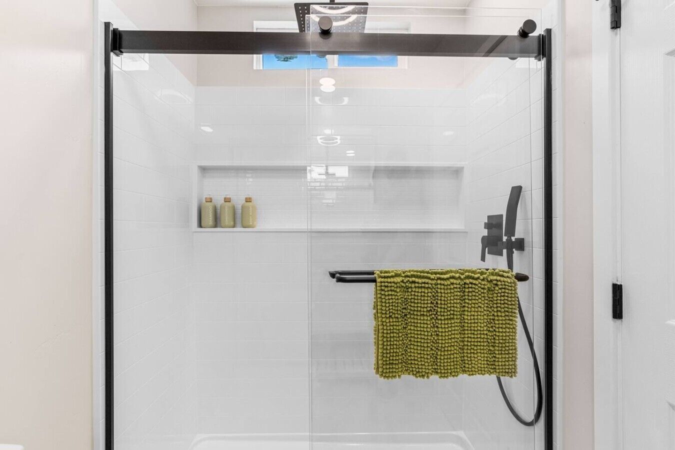 A modern shower enclosure with a glass door, a towel rack, and a shelf with toiletries.