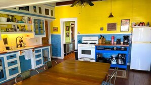 A dining area with a wooden table and chairs, a kitchen with a stove and refrigerator, and a blue and yellow color scheme.