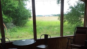 A room with a wooden floor, a round table with chairs, and large windows offering a view of a green field.