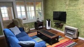 A living room with a blue sofa, a wooden coffee table, a TV, a heater, and a window with blinds.