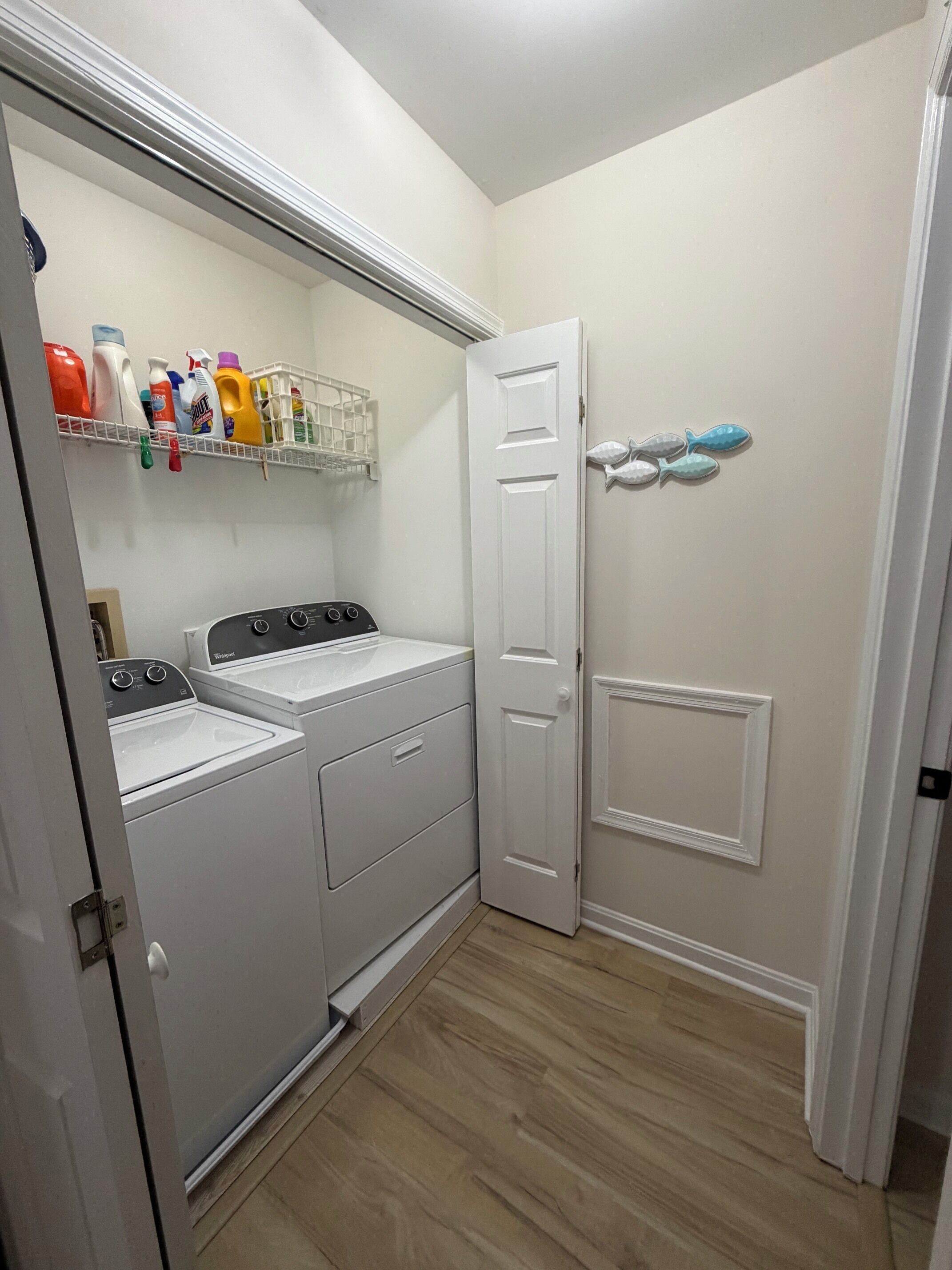 Un cuarto de lavandería con dos lavadoras, un estante con productos de limpieza y una puerta decorada con peces.