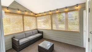 A sunroom with a gray sectional sofa, a small coffee table, and string lights. - Bethany Coastal Retreat, Fully Updated Home, Pool Access & under 1 mile to Beach (Bethany Beach)