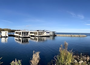A houseboat docked at a pier with a clear view of the water and distant shoreline.