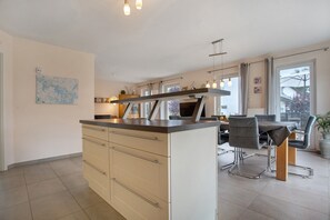 Uma cozinha moderna com uma ilha central, área de refeições com mesa e cadeiras, e uma janela ampla que proporciona luz natural.