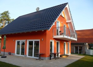 Ein zweistöckiges Haus mit geneigtem Dach, großen Fenstern und einem Balkon.