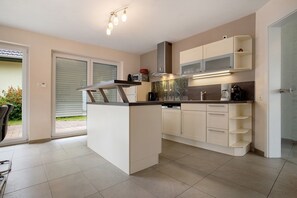 Cozinha moderna com ilha central, armários brancos e vista para o exterior.