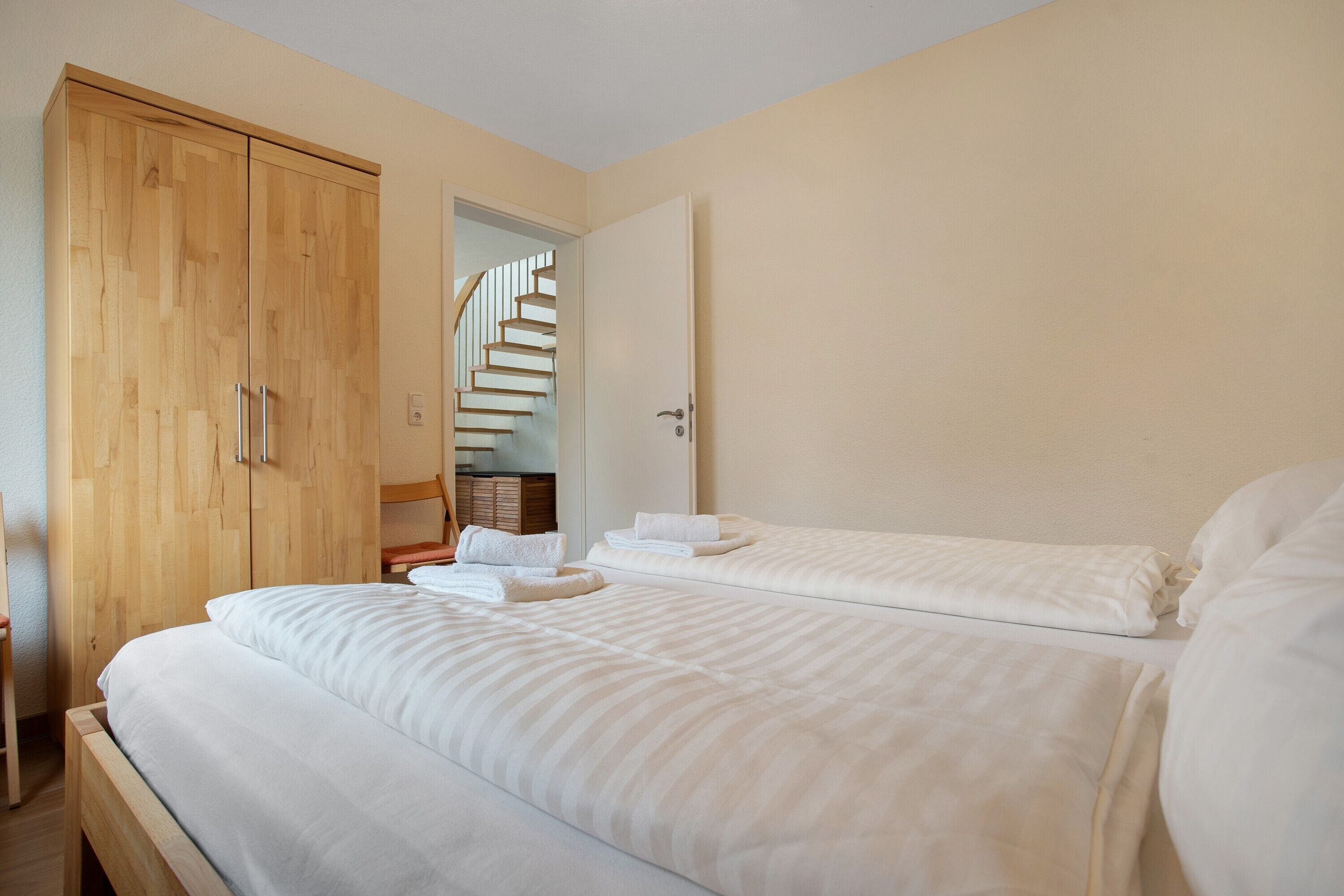 A bedroom with a large bed, a wooden wardrobe, and a staircase leading to an upper floor.