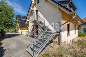 Ein Wohngebäude mit einer Metalltreppe zu einem Balkon, einer gepflasterten Auffahrt und einem Nachbarhaus.