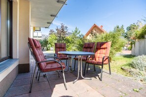 An outdoor patio with four cushioned chairs and a small round table, surrounded by a concrete floor and a low wall.