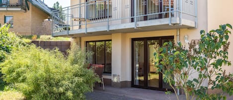 A two-story building with a balcony, a covered patio area, and a garden with various plants.