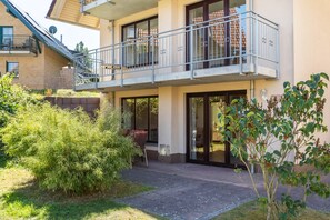 Ein zweistöckiges Gebäude mit einem Balkon, einer überdachten Terrasse und einem Garten mit verschiedenen Pflanzen.