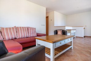 Una sala de estar con un sofá rojo, almohadones a rayas, una mesa de centro de madera y un sillón negro.