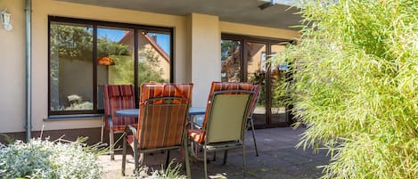 An outdoor seating area with two chairs and a table, a glass door entrance, and a balcony with a railing.