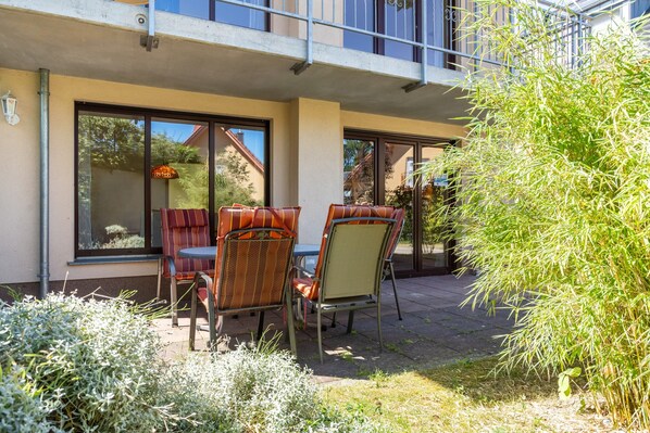 An outdoor seating area with two chairs and a table, a glass door entrance, and a balcony with a railing.