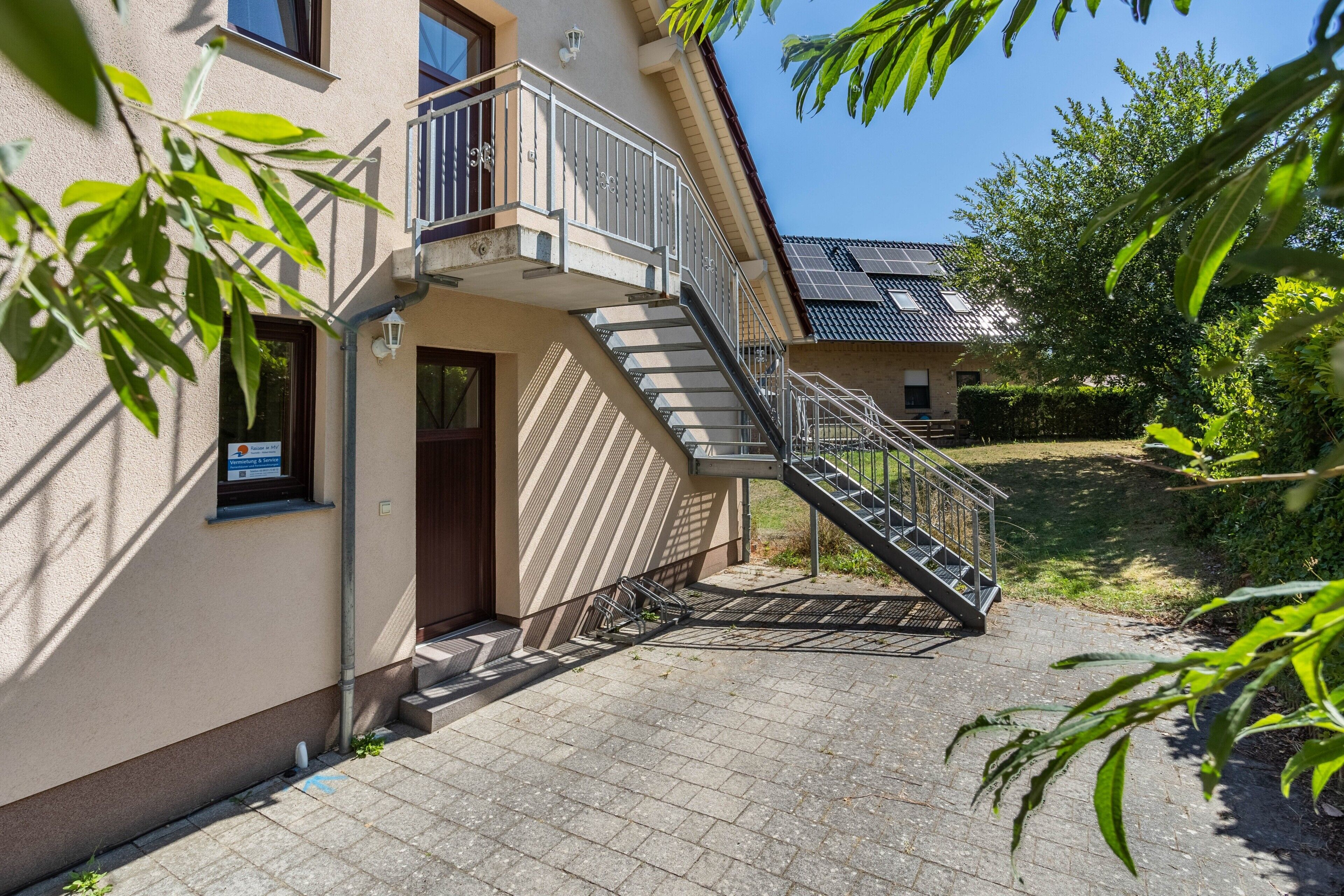 A building with a staircase leading to a second-floor balcony, a door with a sign, and a paved walkway.